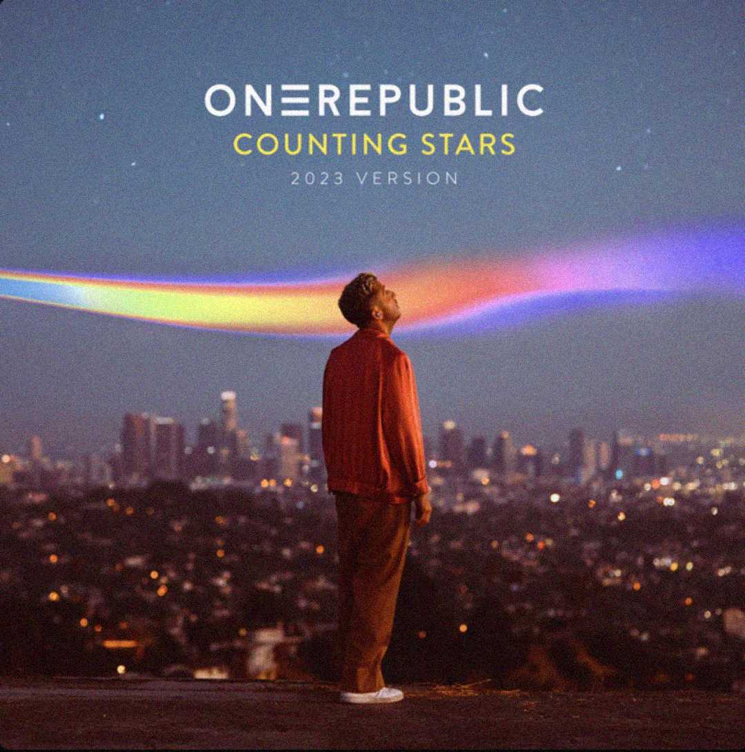 A person stands on a hill overlooking a city at dusk, gazing up at colorful streaks in the sky. Text above reads "OneRepublic Counting Stars 2023 Version.
