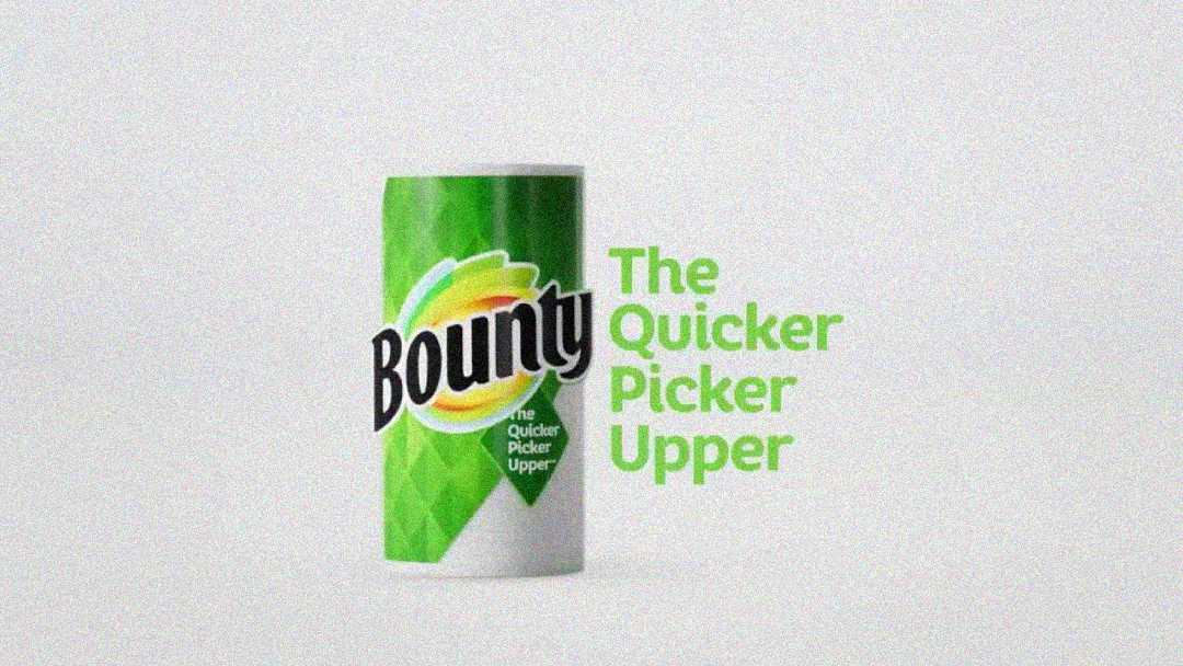 A roll of Bounty paper towels with green packaging sits next to the slogan "The Quicker Picker Upper" in light green text on a white background.