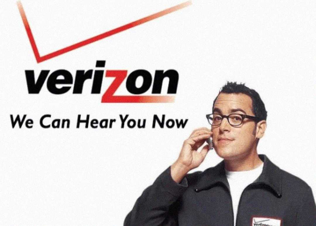 A man wearing glasses and a Verizon jacket holds a phone to his ear, standing next to the Verizon logo and the slogan "We Can Hear You Now" on a white background.