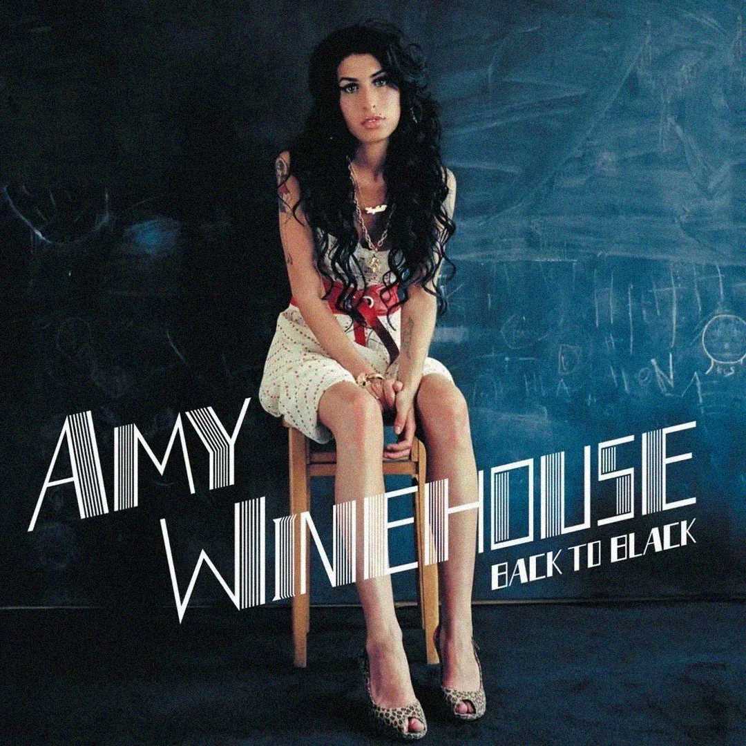A woman with long dark hair sits on a wooden chair against a chalkboard wall. Text on the image reads "Amy Winehouse Back to Black." The scene has a moody, vintage atmosphere.