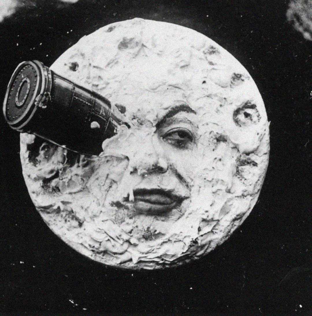 A black-and-white image of the moon with a human face, showing a rocket lodged in one eye, resembling a famous scene from the 1902 silent film "A Trip to the Moon.