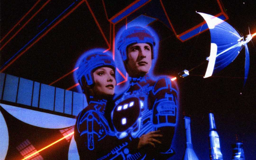 Two people in futuristic, glowing suits stand close together in a digital, neon-lit environment with geometric shapes and a flying disc in the background, evoking a science fiction or virtual reality setting.