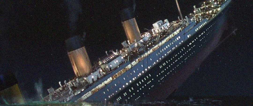 A large ocean liner is tilted steeply in the water at night, with lights still on and smoke coming from its funnels, depicting the ship sinking.