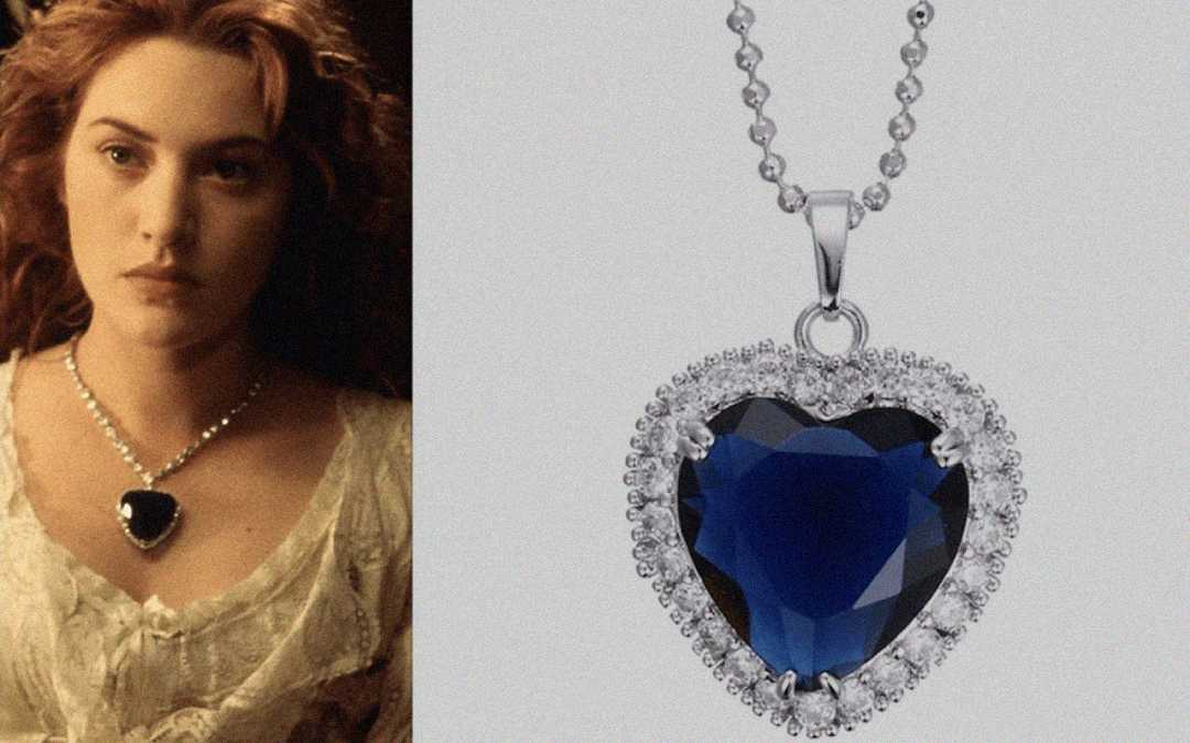A woman with wavy auburn hair wears a white dress and a heart-shaped blue gemstone necklace. Next to her is a close-up of the same necklace, featuring a blue heart-shaped gem surrounded by diamonds on a silver chain.