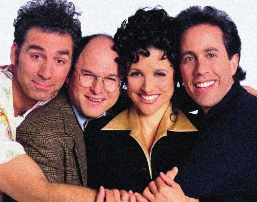 Four people, two men on the left, a woman in the center, and a man on the right, are smiling and posing closely together against a plain background.