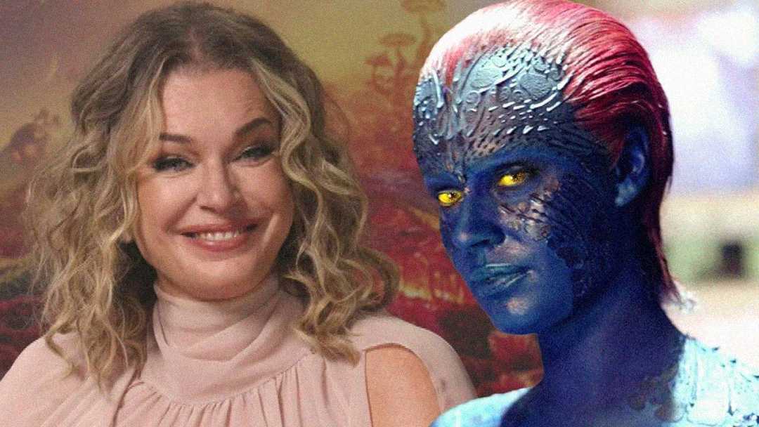 A woman with wavy blonde hair and a light pink blouse smiles next to a blue-skinned fictional character with red hair, yellow eyes, and textured facial patterns.