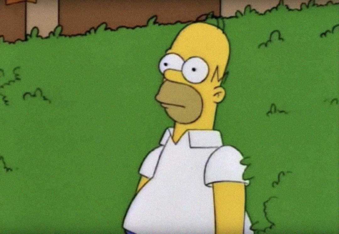 Cartoon character in a white polo shirt stands in front of green bushes, looking startled, from the show "The Simpsons." The character appears to be slowly backing into the bushes.
