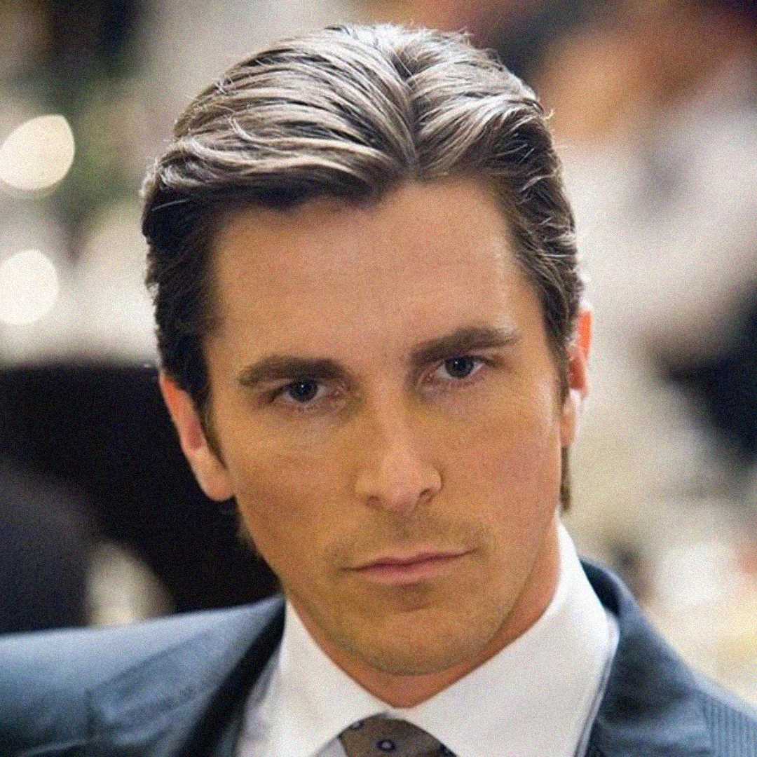 A man with neatly styled brown hair and a serious expression is wearing a suit and tie, looking directly at the camera against a blurred background.