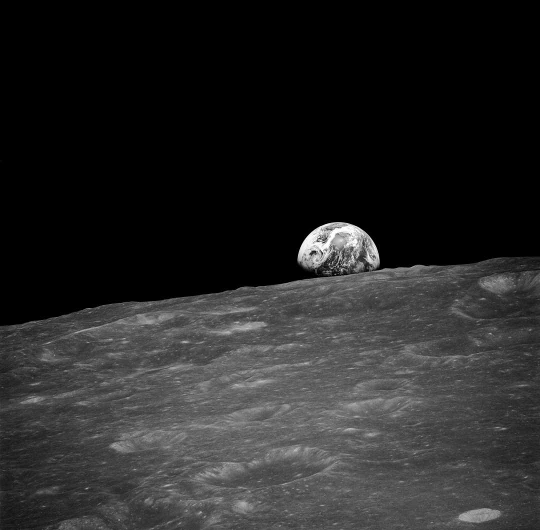 The Earth rises above the rugged, cratered surface of the Moon, set against the blackness of space.