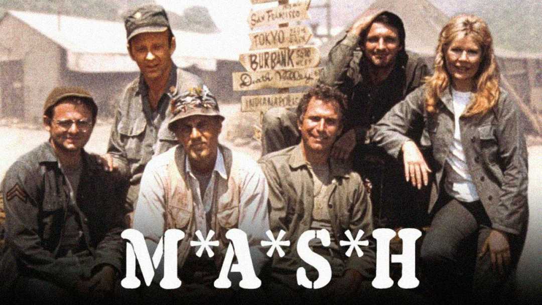 Six people in military clothing sit and kneel together in front of tents and a signpost, with the word “M*A*S*H” in bold white letters across the bottom of the image.