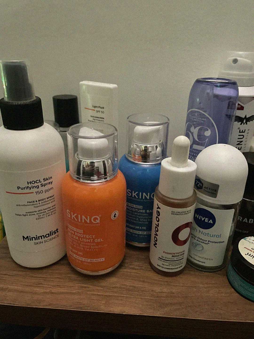 A variety of skincare products, including bottles, pumps, and dropper containers, are grouped on a surface. Visible brands include Minimalist, SKINQ, Nivea, and Novology. The products come in different colors and sizes.