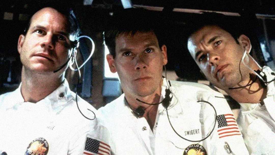 Three astronauts in white NASA spacesuits with American flag patches and headsets sit closely together inside a spacecraft, looking intently ahead. The atmosphere appears tense and focused.