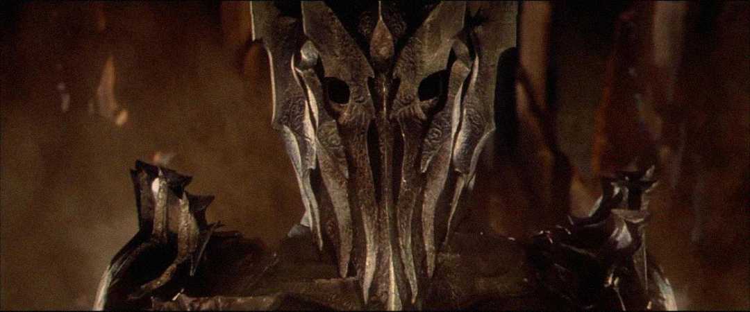 A close-up of a menacing armored figure wearing a spiked metallic helmet with dark eye slits, set against a dim, fiery background.