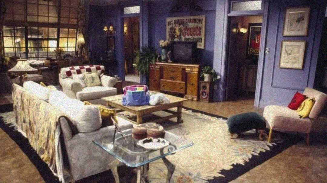 A cozy living room with purple walls, vintage furniture, a white couch, coffee table, TV on a wooden dresser, wall art, and a large rug. Sunlight streams through a window on the left, creating a warm atmosphere.