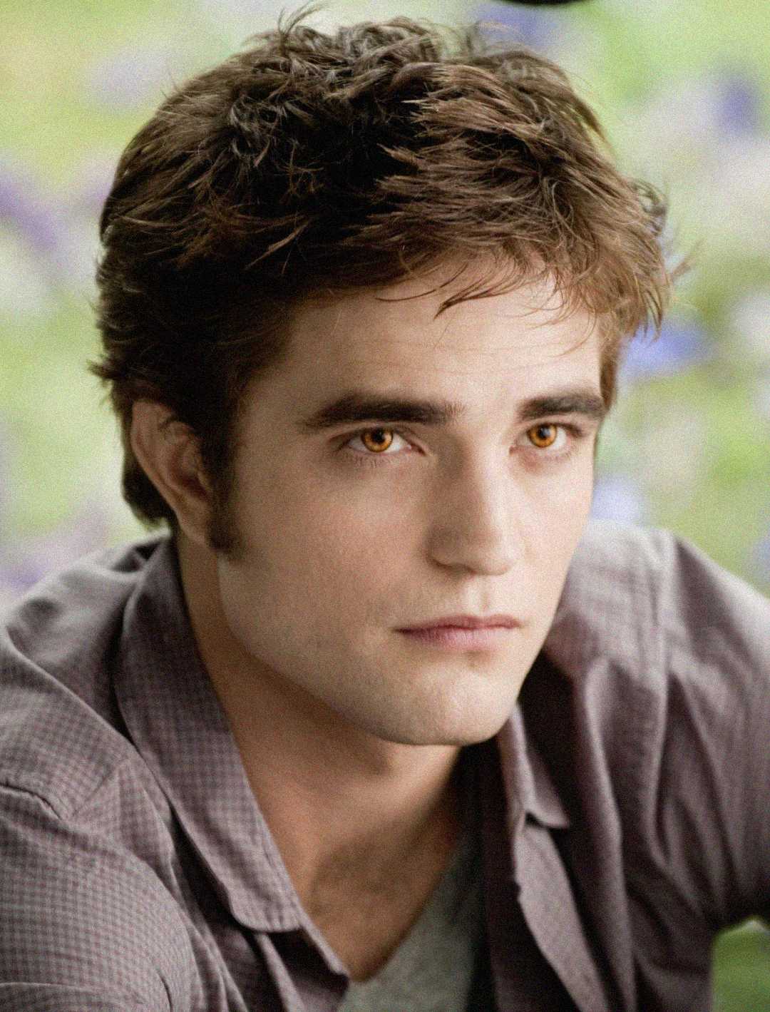 Young person with tousled brown hair and pale skin gazes thoughtfully forward. They wear a gray shirt, and the soft, blurred green and purple background suggests an outdoor setting.