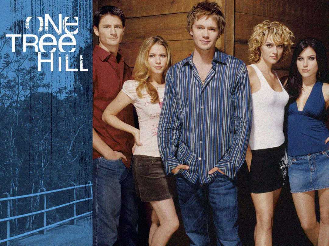 Five young adults stand together posing for a promotional image for the TV show "One Tree Hill." The show's title appears on the left, with a blue-toned background featuring trees and a bridge.