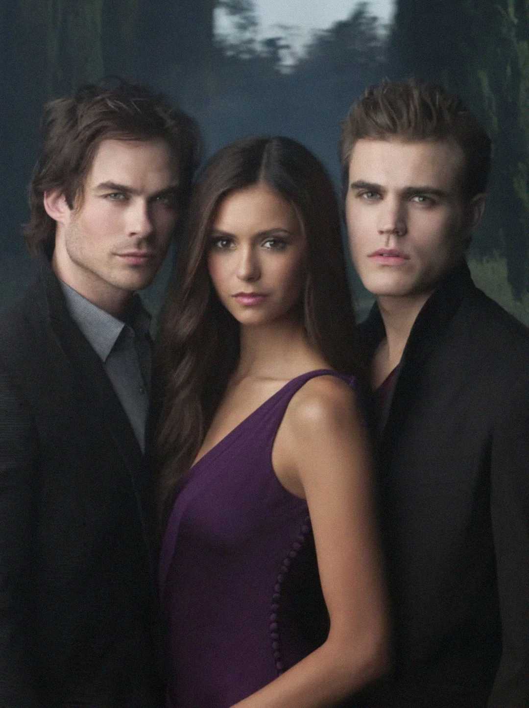 Three young adults stand closely together. The woman in the center wears a sleeveless purple dress, flanked by two men in dark suits, all gazing seriously at the camera against a dark, blurred outdoor background.