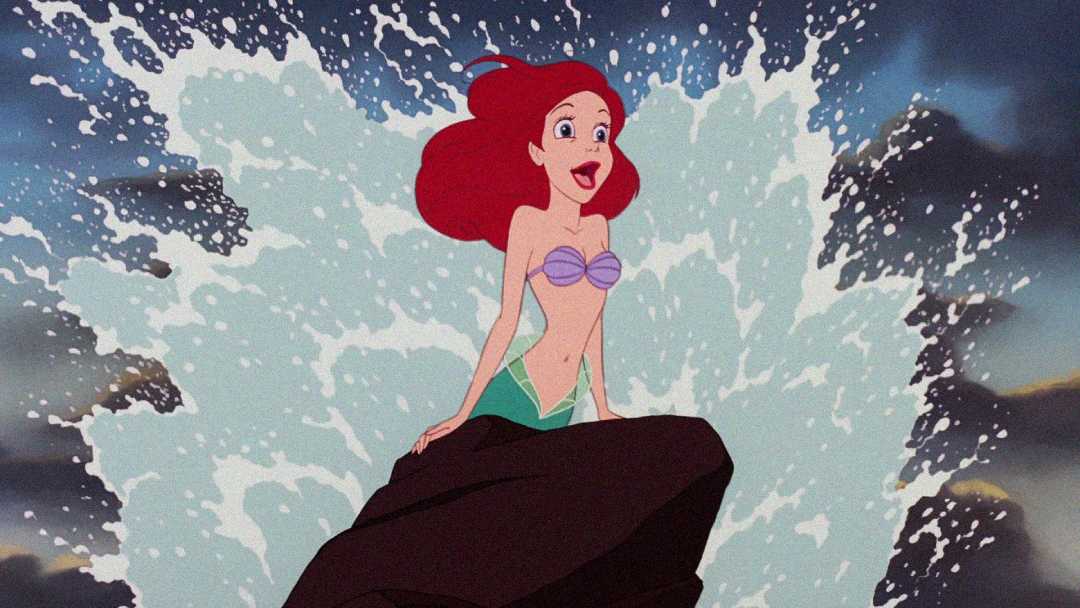 Animated red-haired mermaid with a purple seashell top sits on a rock as ocean waves splash dramatically behind her, against a dark, cloudy sky.