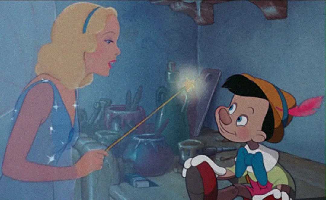 A blonde fairy in a blue dress holds a glowing wand, speaking to Pinocchio, a wooden puppet boy with a hat and red feather, in a cozy, cluttered workshop.
