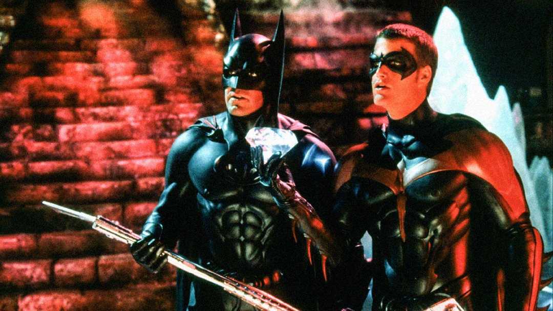 Batman and Robin stand side by side in their costumes, holding a glowing diamond and staff, with a red-lit stone staircase in the background.