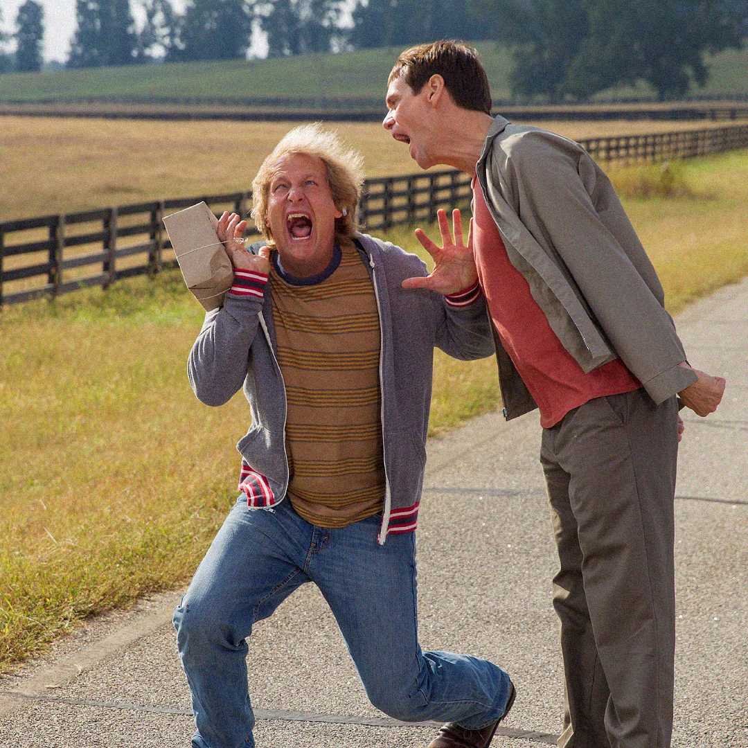 Two men on a rural road; one is screaming and holding a paper bag, looking startled, while the other leans toward him, yelling animatedly. A wooden fence and fields are visible in the background.