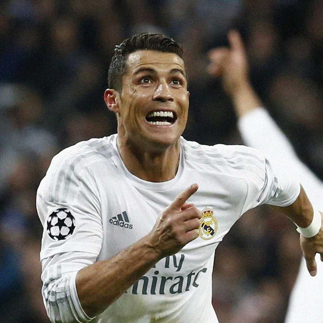 A soccer player in a white Real Madrid jersey celebrates energetically, smiling widely and pointing with his right hand during a match.