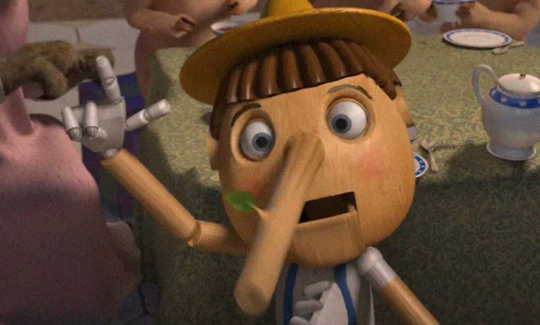A wooden puppet with a long nose, wearing a yellow hat, looks surprised while sitting at a table set for tea. A green leaf is stuck to his nose and his mouth is open in shock.
