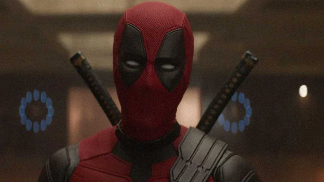 A person in a red and black mask and suit stands indoors with two swords strapped to their back. The background is dimly lit and slightly blurred with circular blue lights visible behind them.