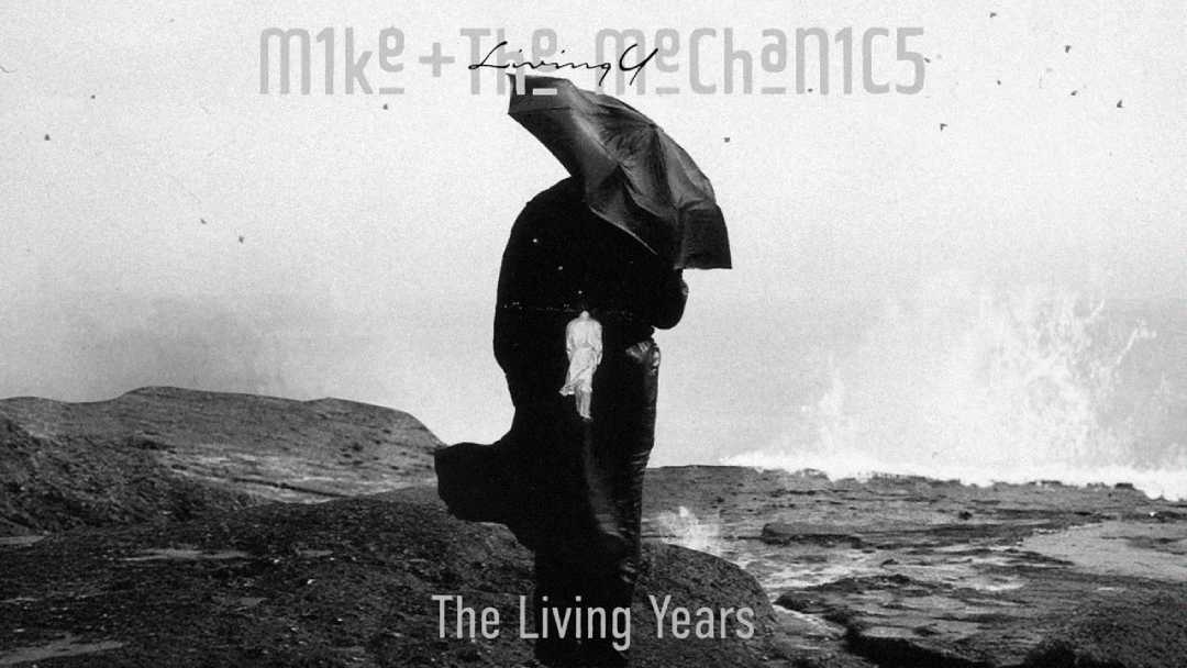 A person stands on a rocky shore facing the sea, holding an umbrella against strong wind and waves. The grayscale image includes the text "Mike + The Mechanics" and "The Living Years.