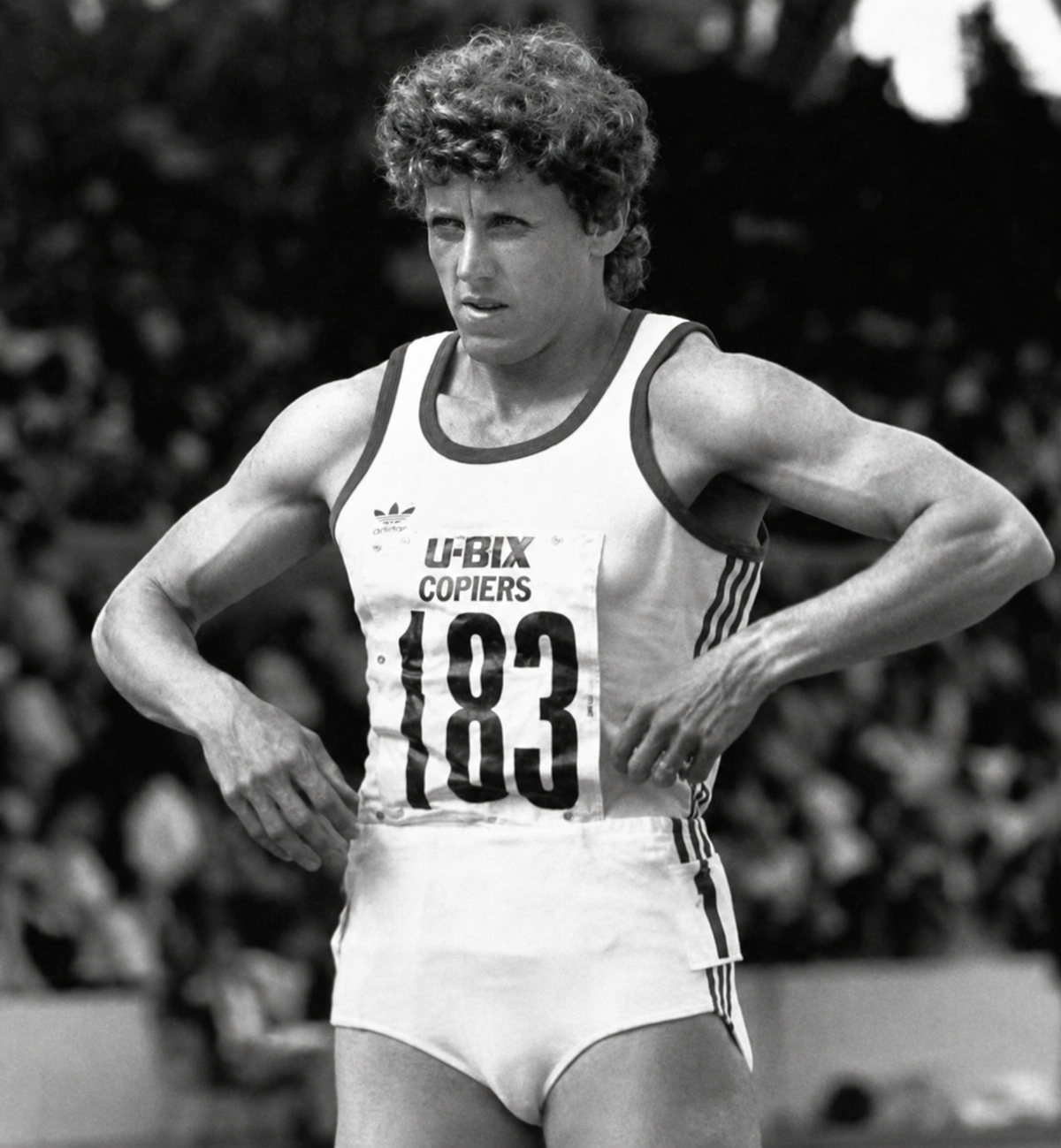 A track and field athlete wearing a running uniform with the number 183 adjusts their shorts, standing on a track with a blurred crowd in the background. The image is black and white. 14. Jarmila Kratochvilova’s 1:53.28 in the Women’s 800 Meters