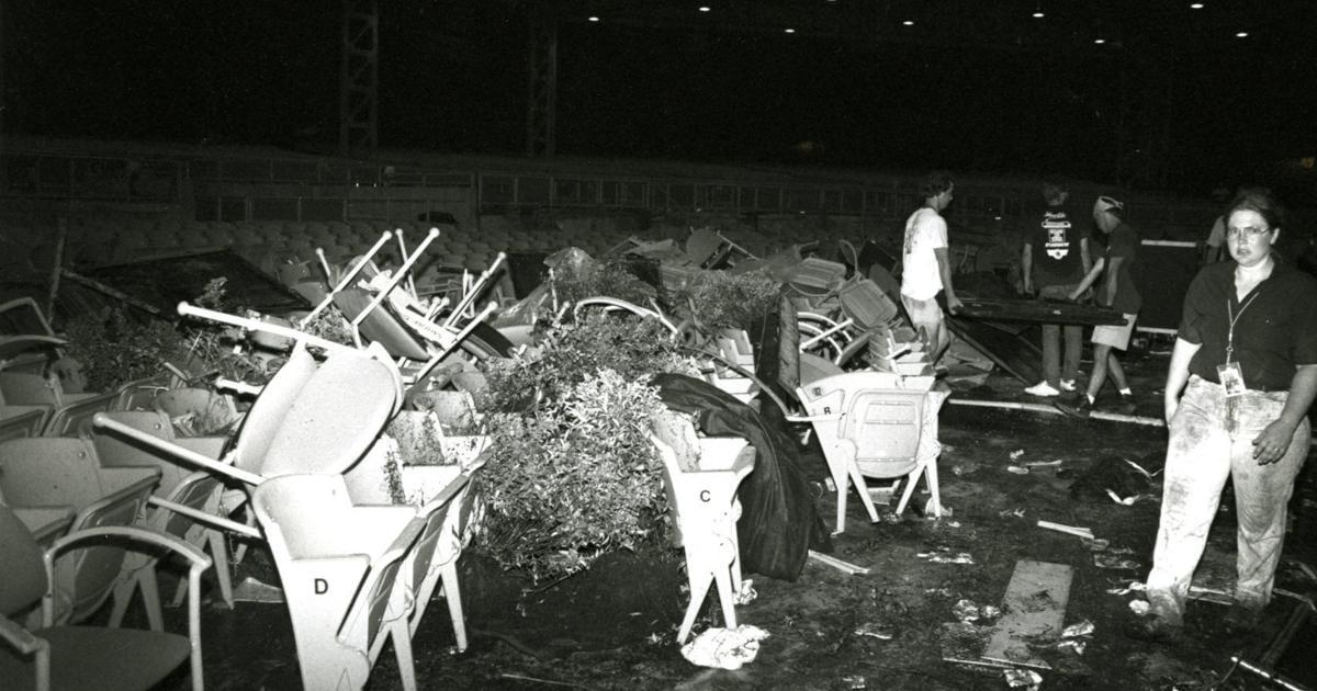 A black-and-white photo showing a chaotic scene with overturned chairs, scattered debris, and a few people standing among the mess in what appears to be an indoor venue or theater.