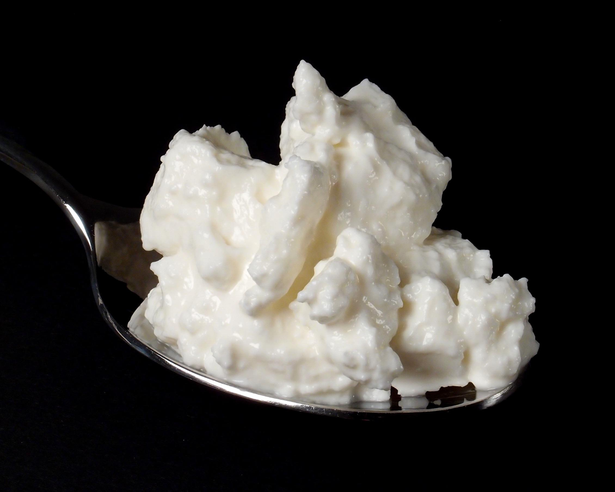 A close-up of a metal spoon holding a serving of white, chunky cottage cheese against a solid black background.