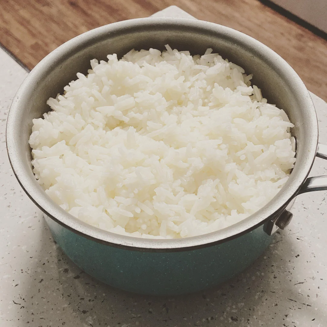 A pot filled with freshly cooked white rice sits on a light-colored kitchen countertop.