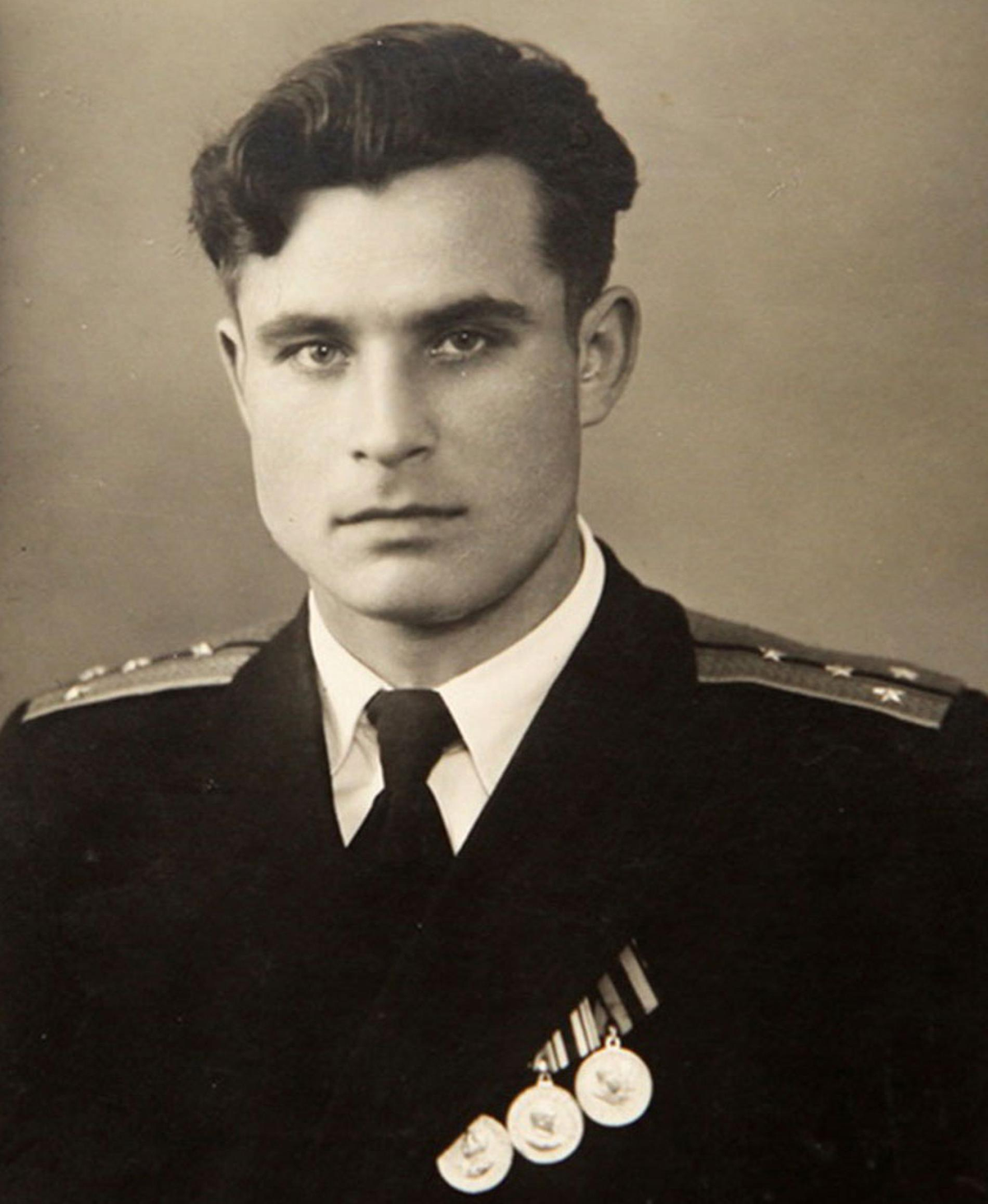 A young man in a military uniform with medals on his chest poses for a black-and-white portrait against a plain background. cold war.