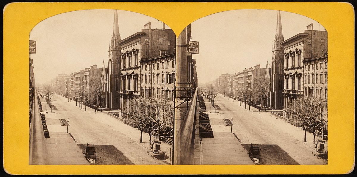 A sepia-toned stereograph shows a quiet city street lined with trees and multi-story brick buildings, including two church spires, viewed from above with sidewalks and empty roads under a clear sky.
