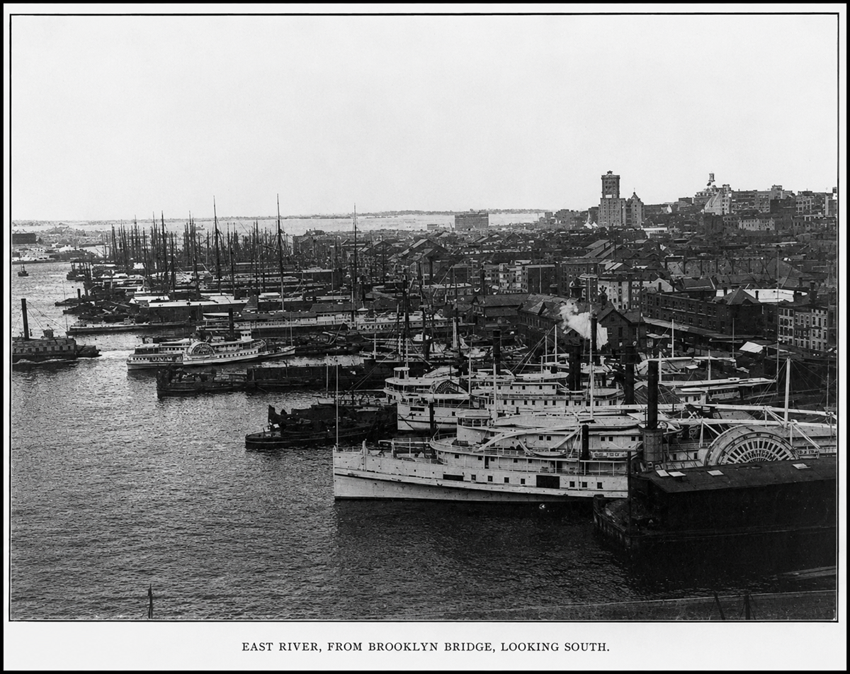 Historic black-and-white photo of ships docked along the East River with buildings lining the waterfront; view is from Brooklyn Bridge, looking south.