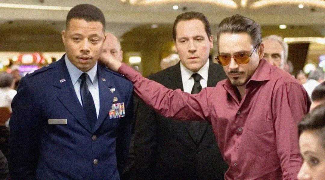 Three men stand together in a casino; one wears a military uniform, another is in a suit, and the third, in a red shirt and tinted glasses, gestures with his arm across the uniformed man's shoulder.