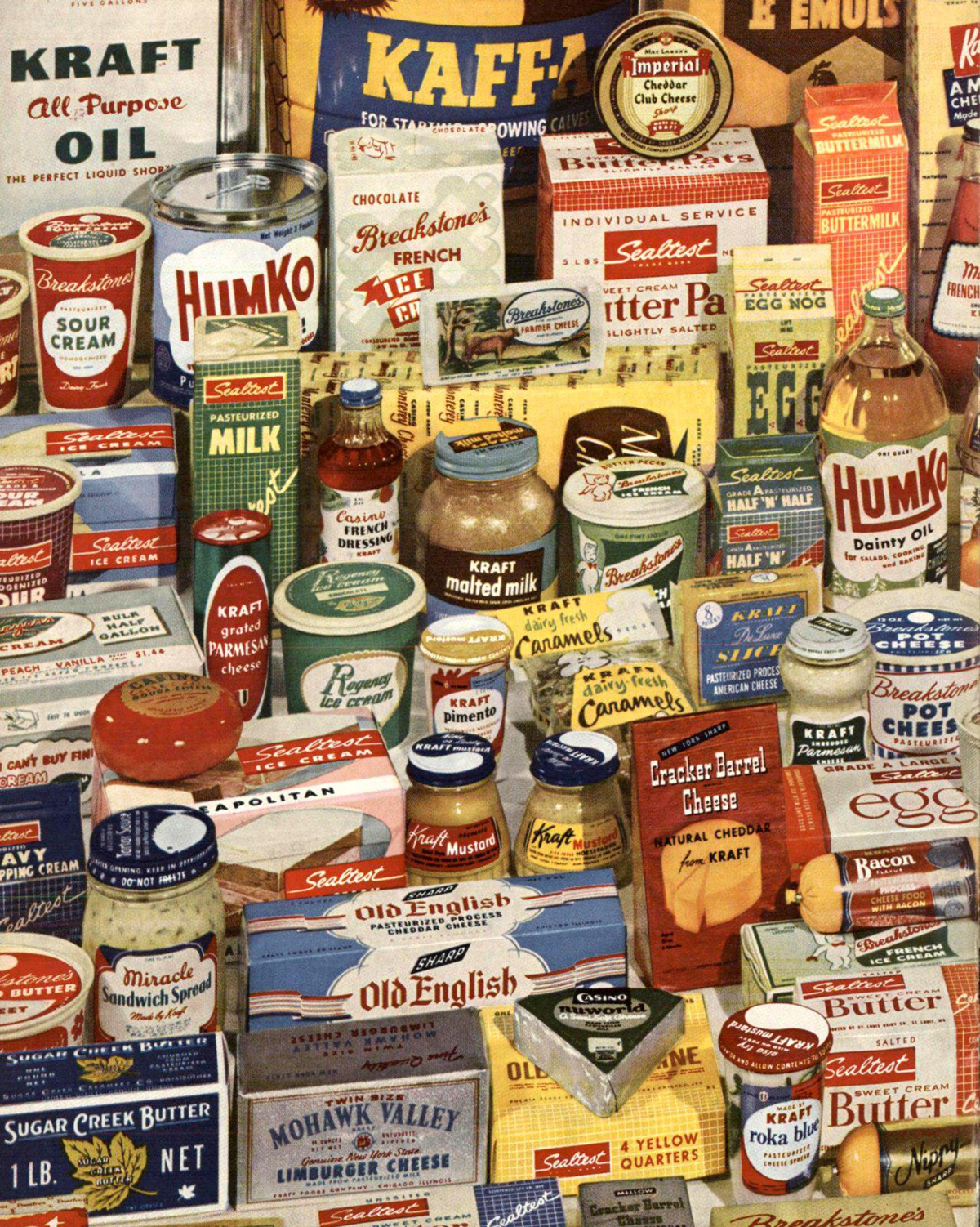 A colorful assortment of vintage grocery products, including canned goods, boxed foods, jars, and tins, with recognizable brands like Kraft, Humko, and Sealtest, arranged closely together in a nostalgic display.