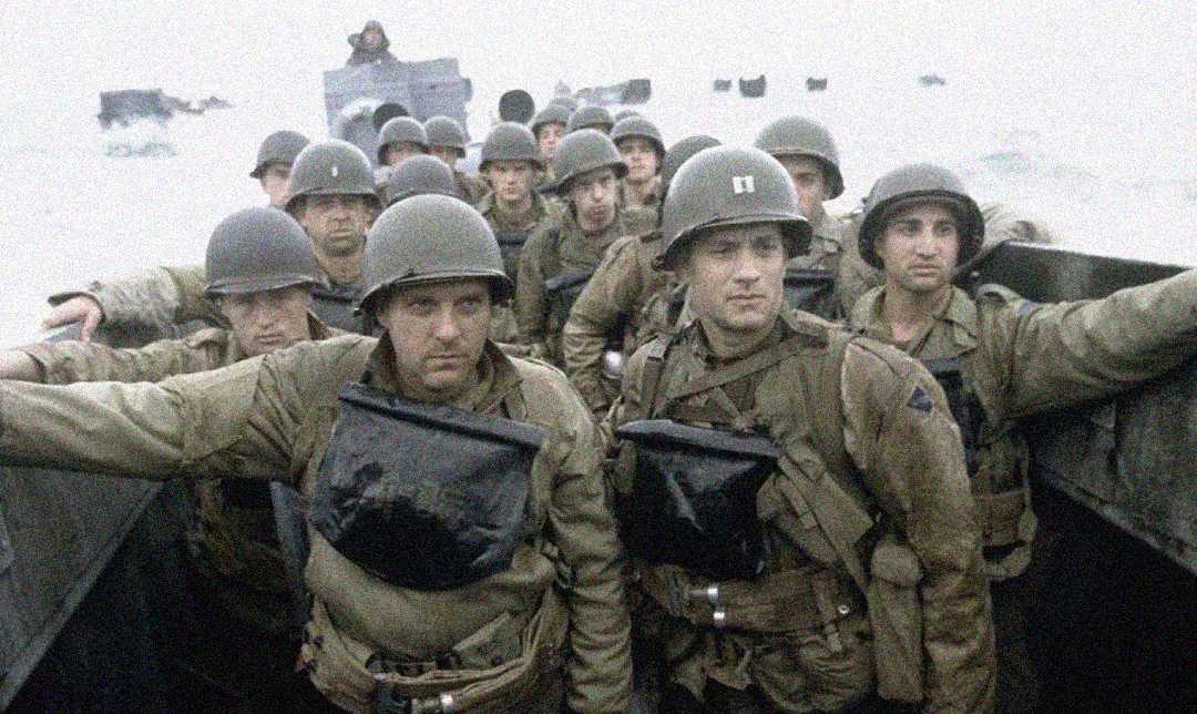 A group of World War II soldiers wearing helmets and military gear stand crowded together in a landing craft, heading toward a beach under overcast skies, with additional landing crafts visible in the background.