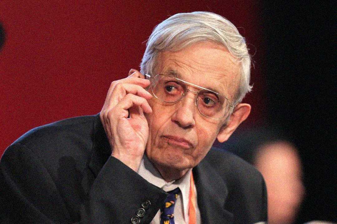 An elderly man with gray hair and glasses, wearing a suit and tie, looks thoughtfully to the side while touching his ear. The background is red and out of focus.