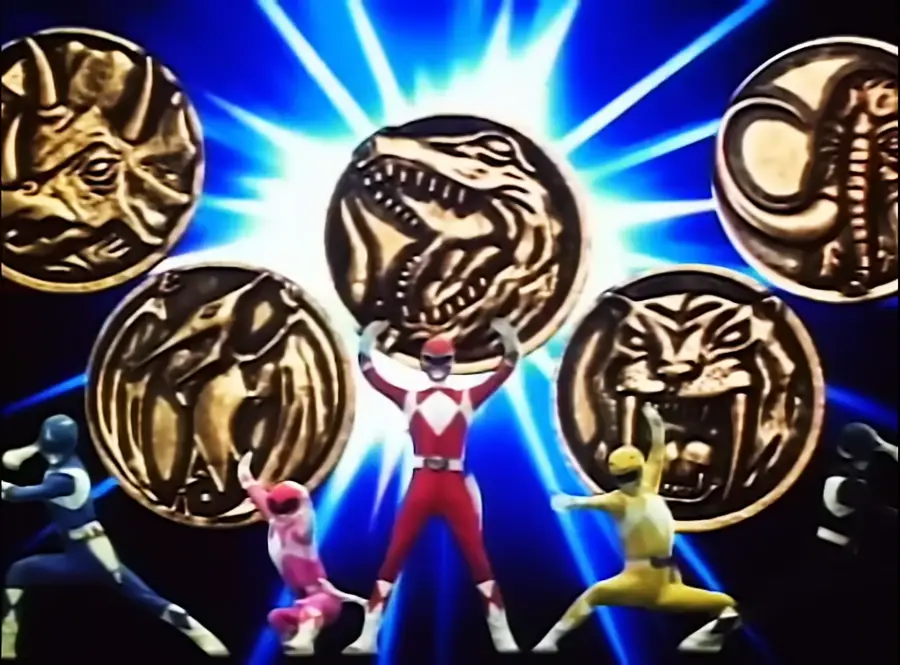 Five Power Rangers pose heroically in front of glowing dinosaur-themed power coins, each coin featuring a different dinosaur symbol, with a dramatic blue and white burst in the background.