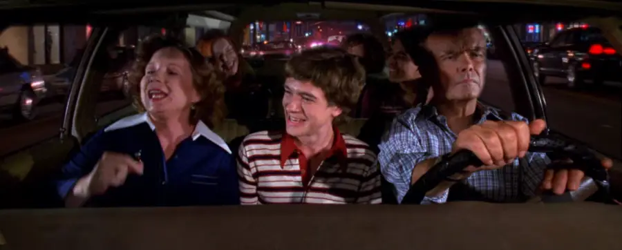 Five people sit in a car at night, enjoying themselves. The driver looks focused, while the others, including a woman and a young man in a striped shirt, appear to be singing and laughing together.