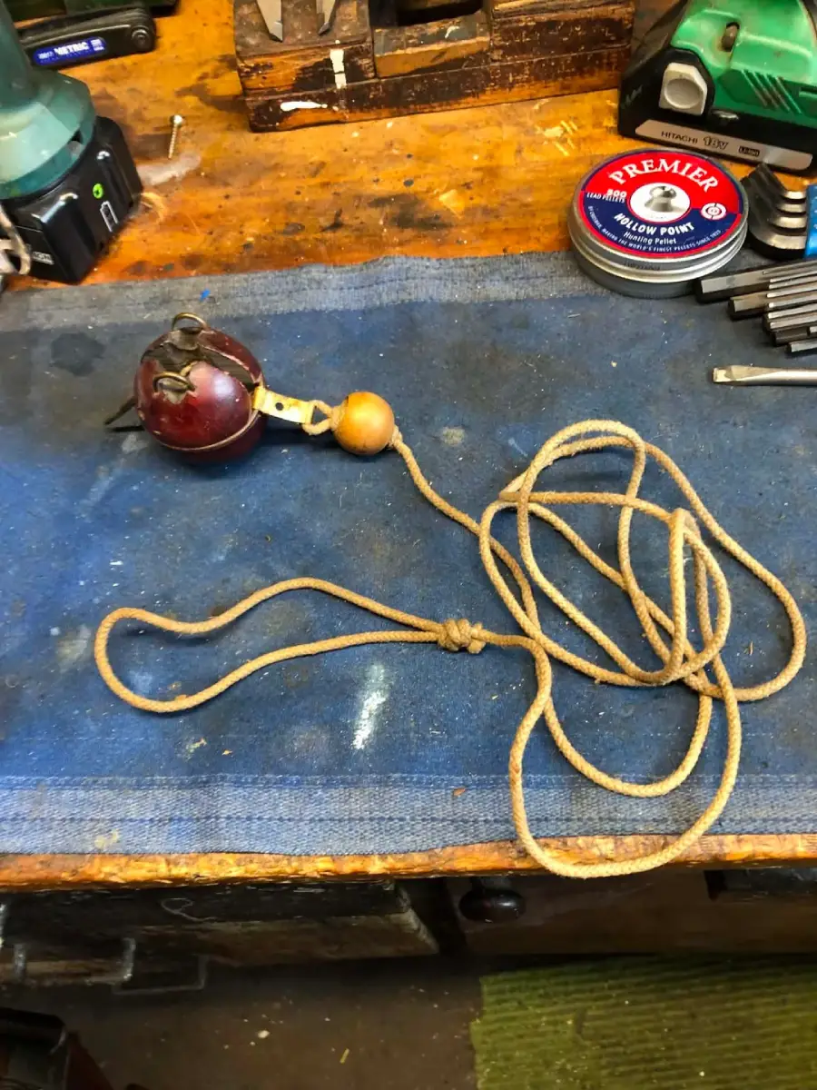 A plumb bob with a wooden handle and a long string rests on a blue work mat. The bench has tools, a tin labeled "Premier," and various items scattered in the background.