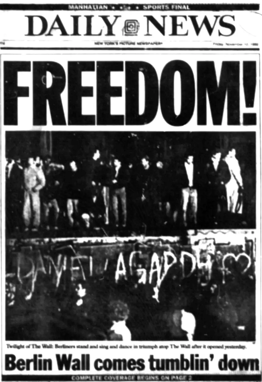 A black-and-white Daily News front page shows people celebrating atop the Berlin Wall under the bold headline “FREEDOM!” with graffiti on the Wall and the subhead “Berlin Wall comes tumblin’ down.”