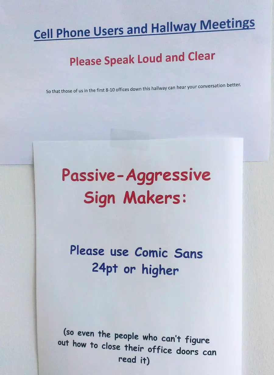 Two printed signs on a wall. The top sign asks cell phone users to speak loudly and clearly. The bottom sign humorously requests passive-aggressive sign makers to use Comic Sans font, 24pt or higher, for readability.
