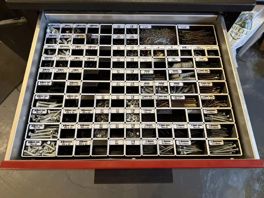 An organized drawer with many small labeled compartments, each filled with different types and sizes of screws, nails, bolts, and fasteners, sorted neatly into sections.