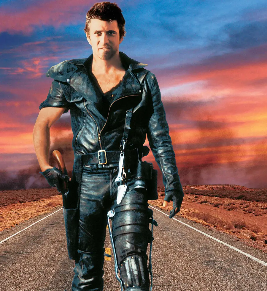 A man in black leather armor walks confidently down an empty road in a desert landscape, with a dramatic sunset sky and clouds in the background.