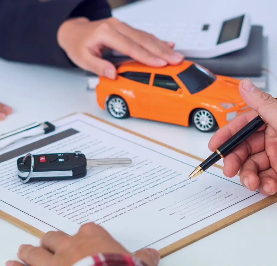 A person holds a pen over a contract on a clipboard, while another hand rests on an orange toy car. A car key and a calculator are also visible on the table, suggesting a car purchase or lease agreement.
