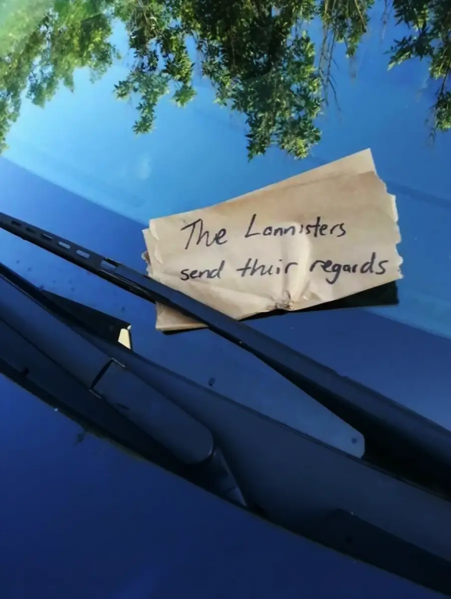 A handwritten note reading "The Lannisters send their regards" is tucked under a car windshield wiper, with tree reflections visible on the windshield.