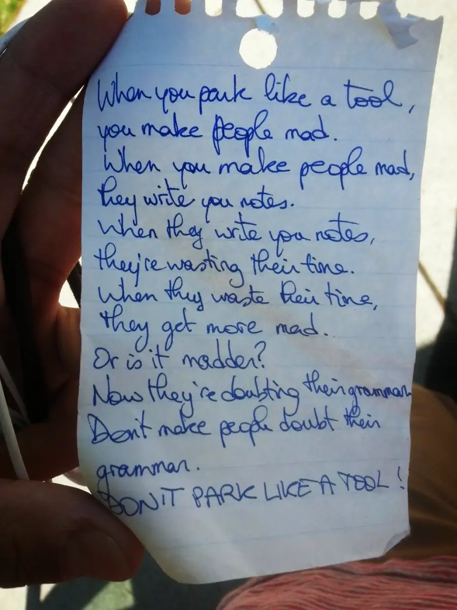 A handwritten note on torn paper held by a person reads: “When you park like a tool, you make people mad. When you make people mad, they write you notes. When they write you notes, they’re wasting their time…” and more.